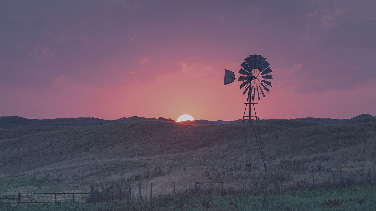 A windmill-driven water pump standing on the horizon during sunsets.