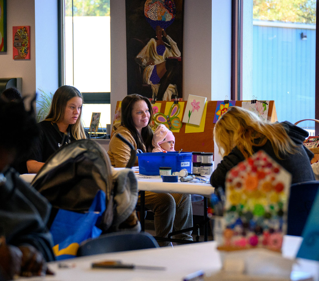 A group of mothers sitting at a table in a classroom, one holding a baby..
