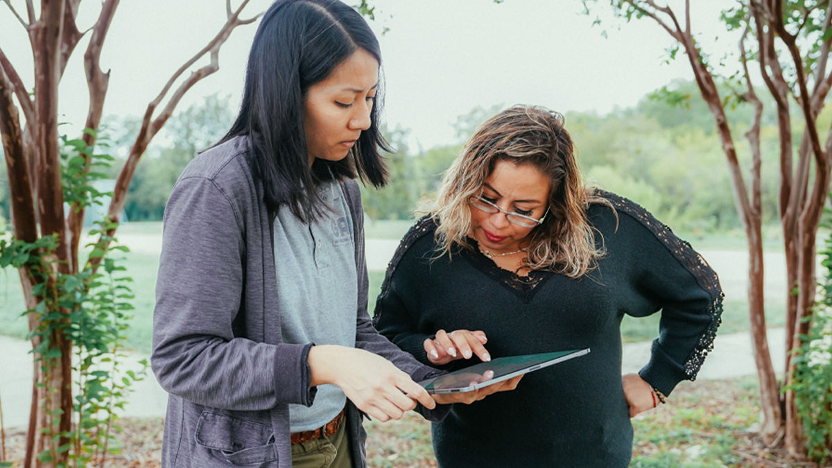 Two woman using a tablet touch pad while standing outside.