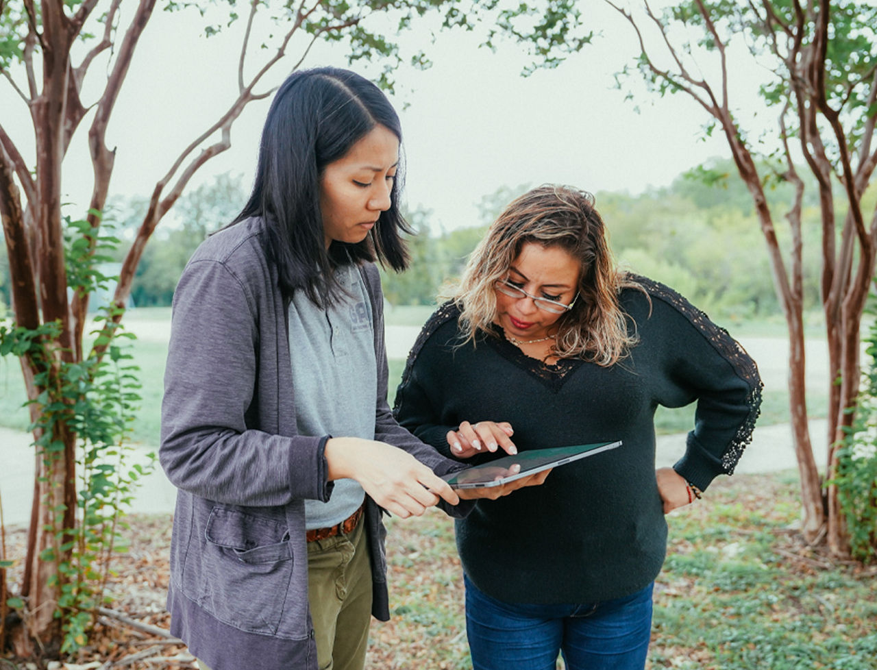 Two woman using a tablet touch pad while standing outside.