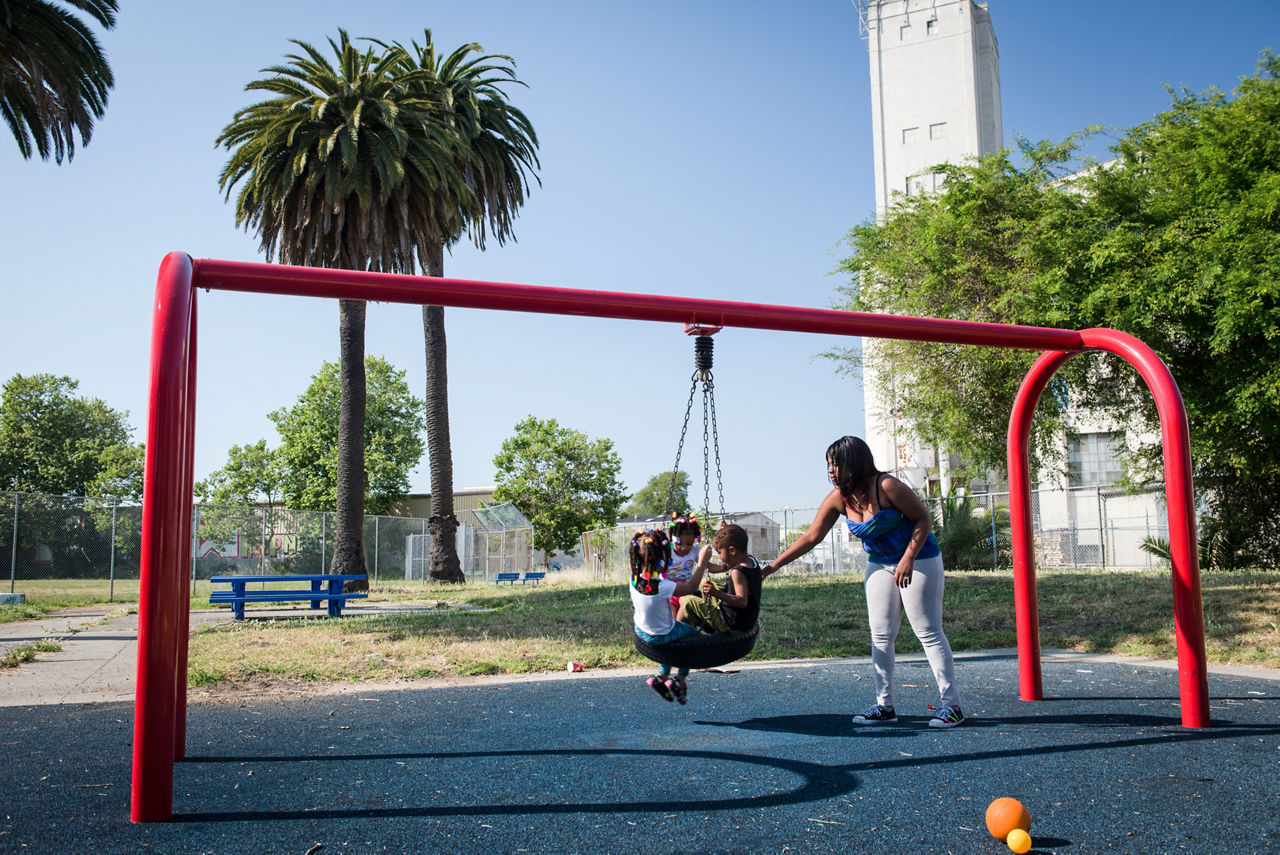 A mother pushing her children on a tire swing in a city park.