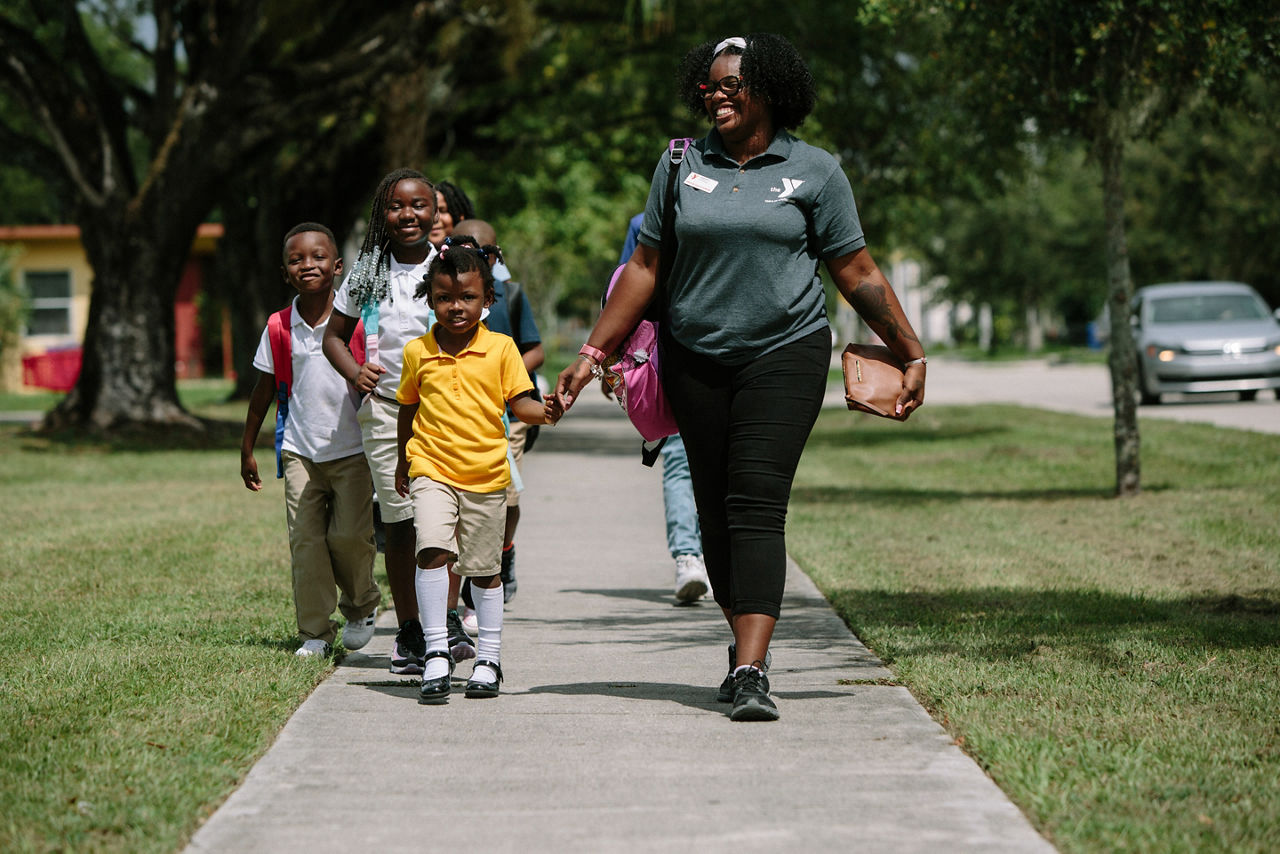 A woman and a class of young children walking on a sidewalk.