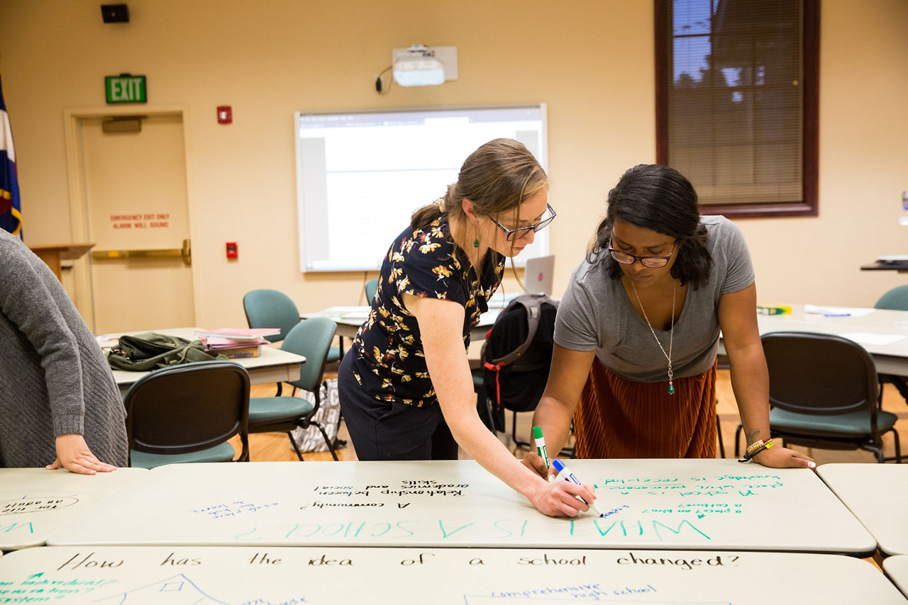 Two woman use colored markers on a white board.