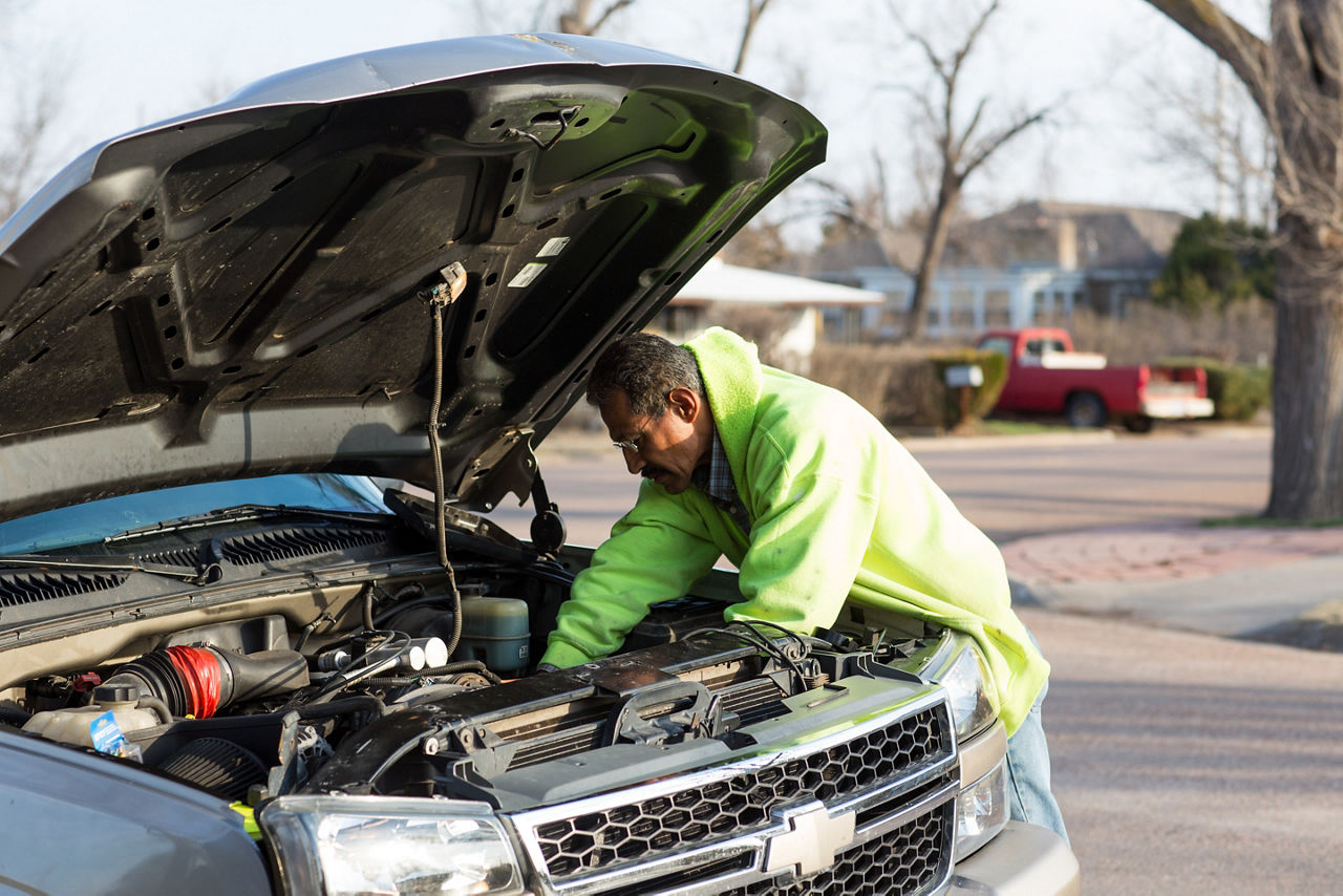 A man repairs a pickup truck motor on a side street.