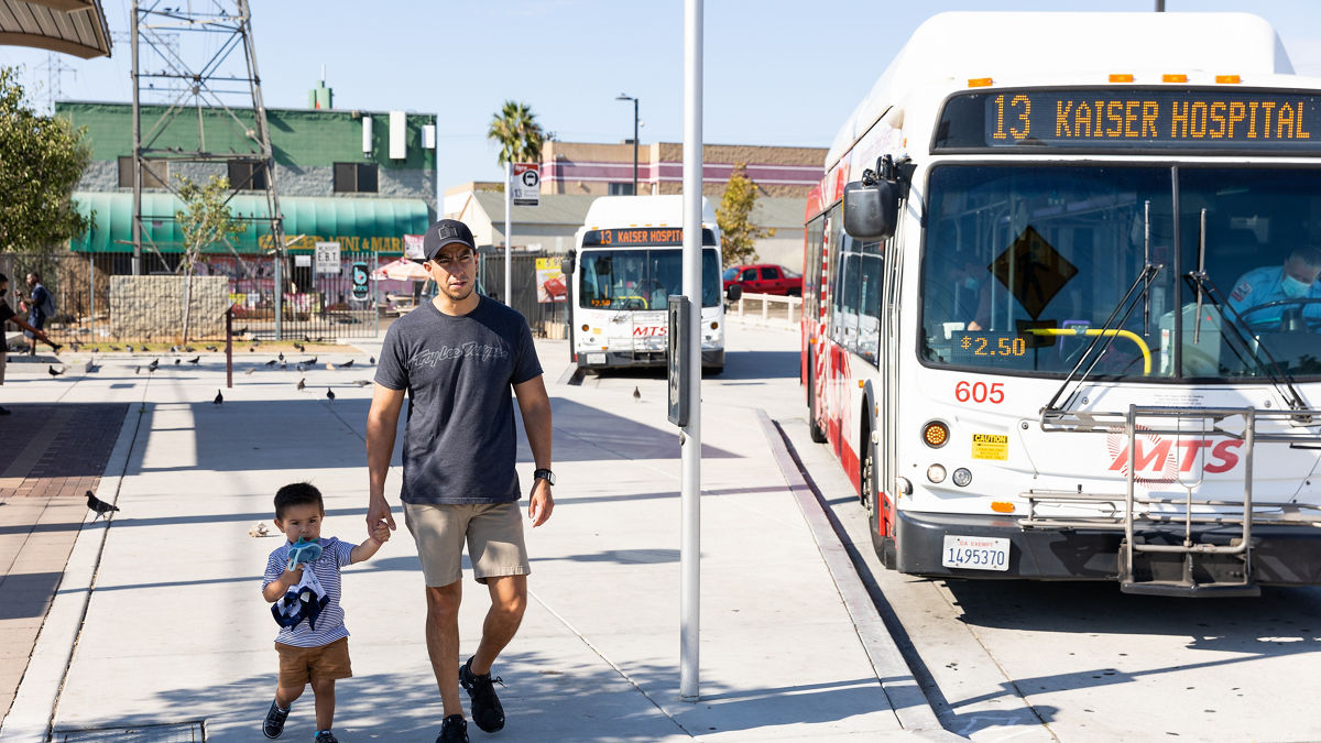 A father and son walking on a sidewalk while a bus passes by.