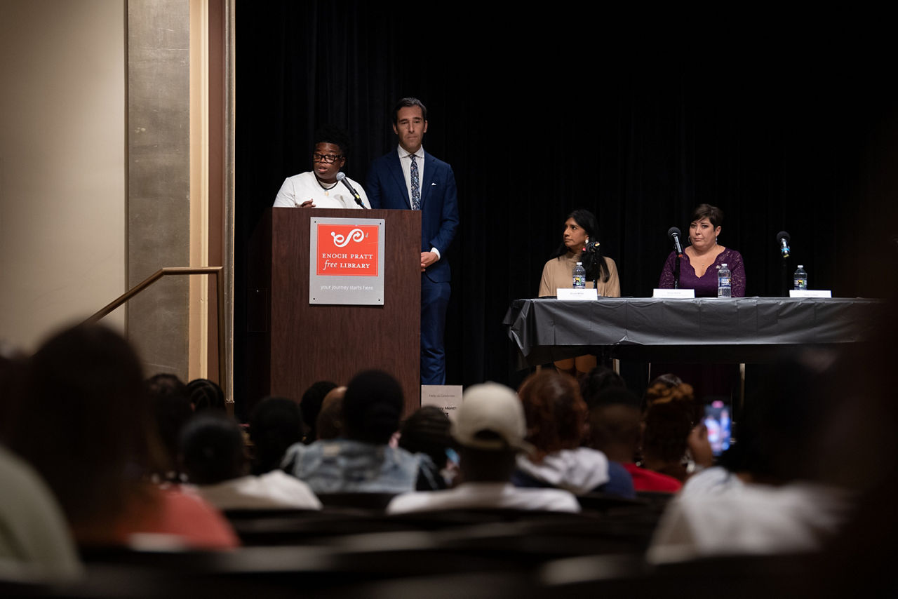 A person speaks from a podium at a town hall meeting.