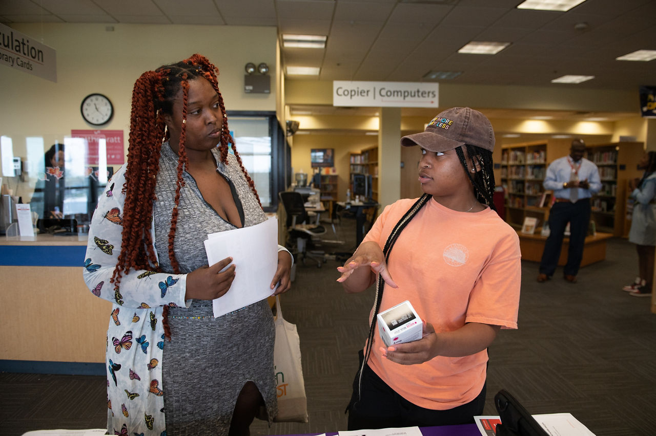 Two women talking about information on a table in a library.