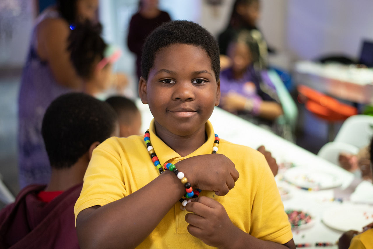 A young boy showing a beaded bracelet and necklace that he made. 