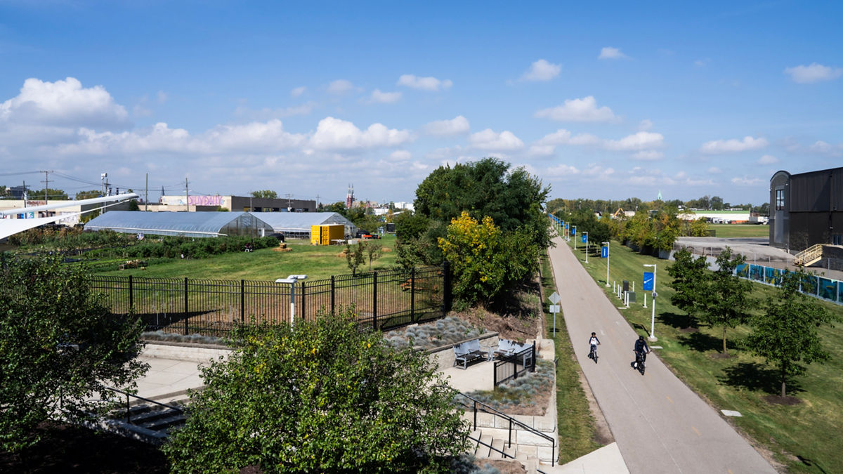 Two people ride bikes along a path next to a small park.