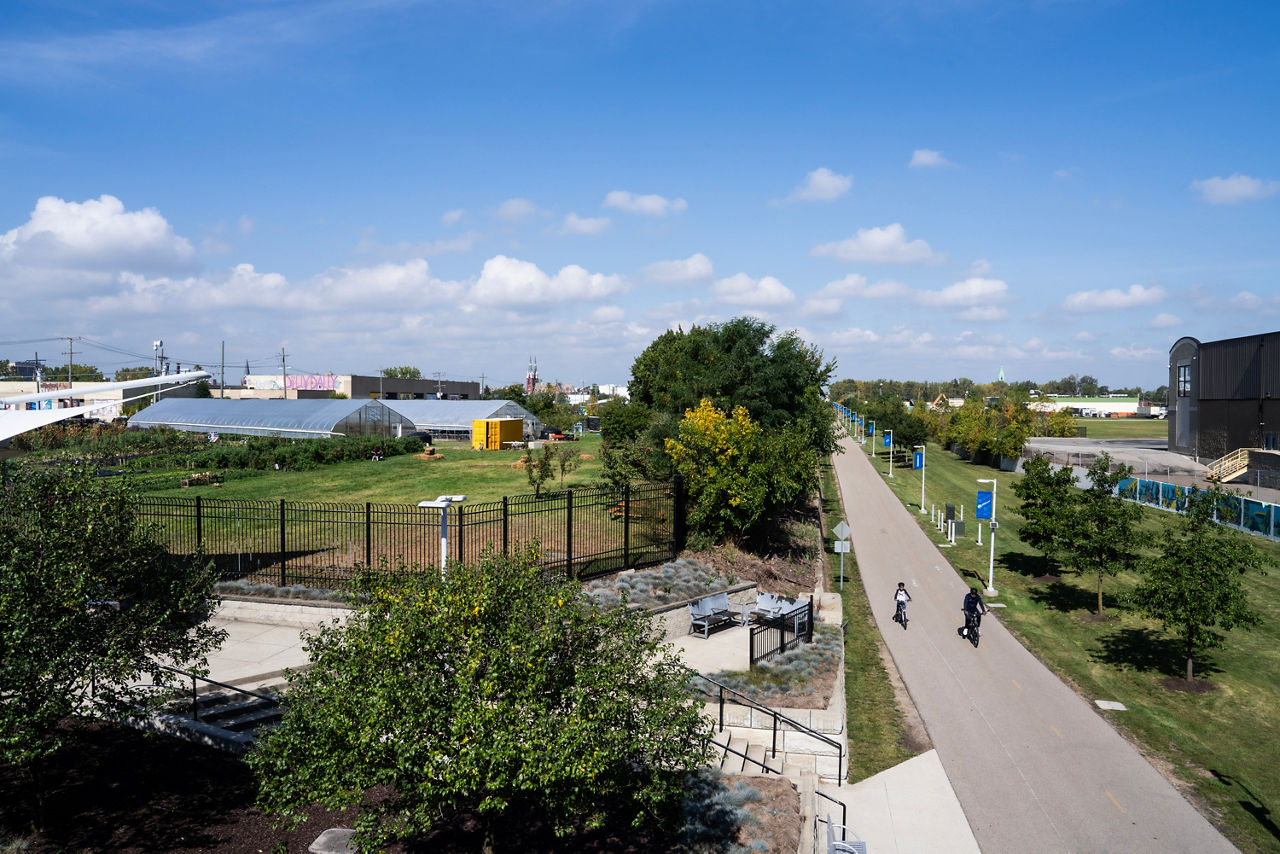 Two people ride bikes along a path next to a small park.