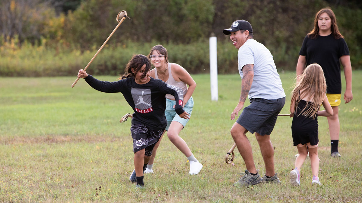 A group of people running on a field with large sticks in their hands.