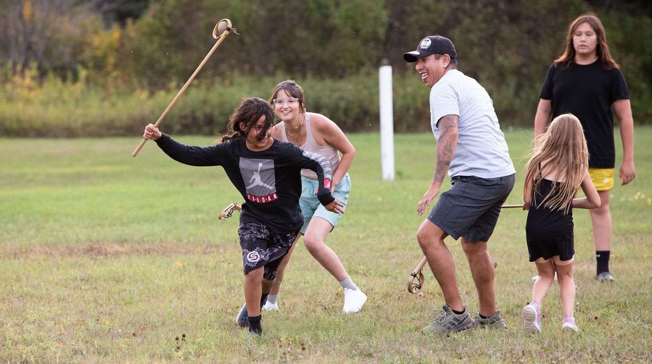 A group of people running on a field with large sticks in their hands.