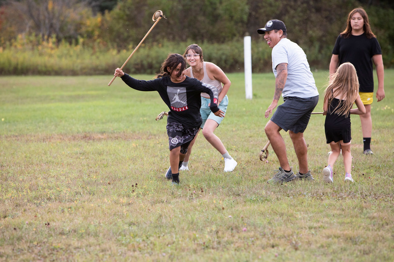 A group of people running on a field with large sticks in their hands.