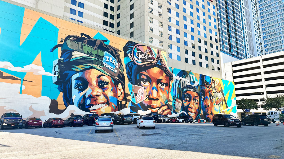 A mural on a city wall depicts a closeup image of four smiling Black children.