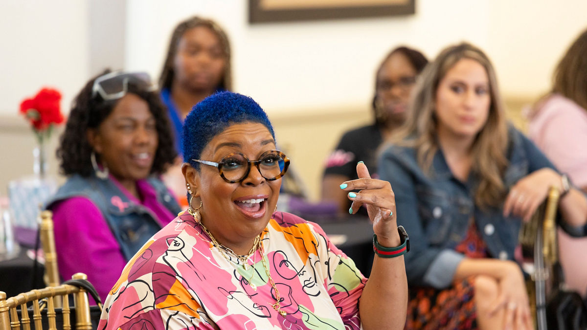 A person with short blue hair wearing scrubs is speaking in a facilitated discussion.