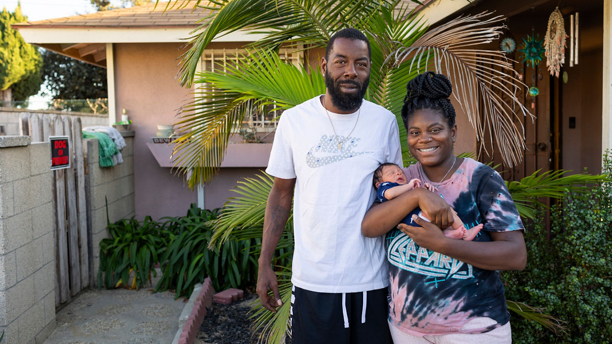 Two parents stand in front of their home in Los Angeles holding their newborn baby. 