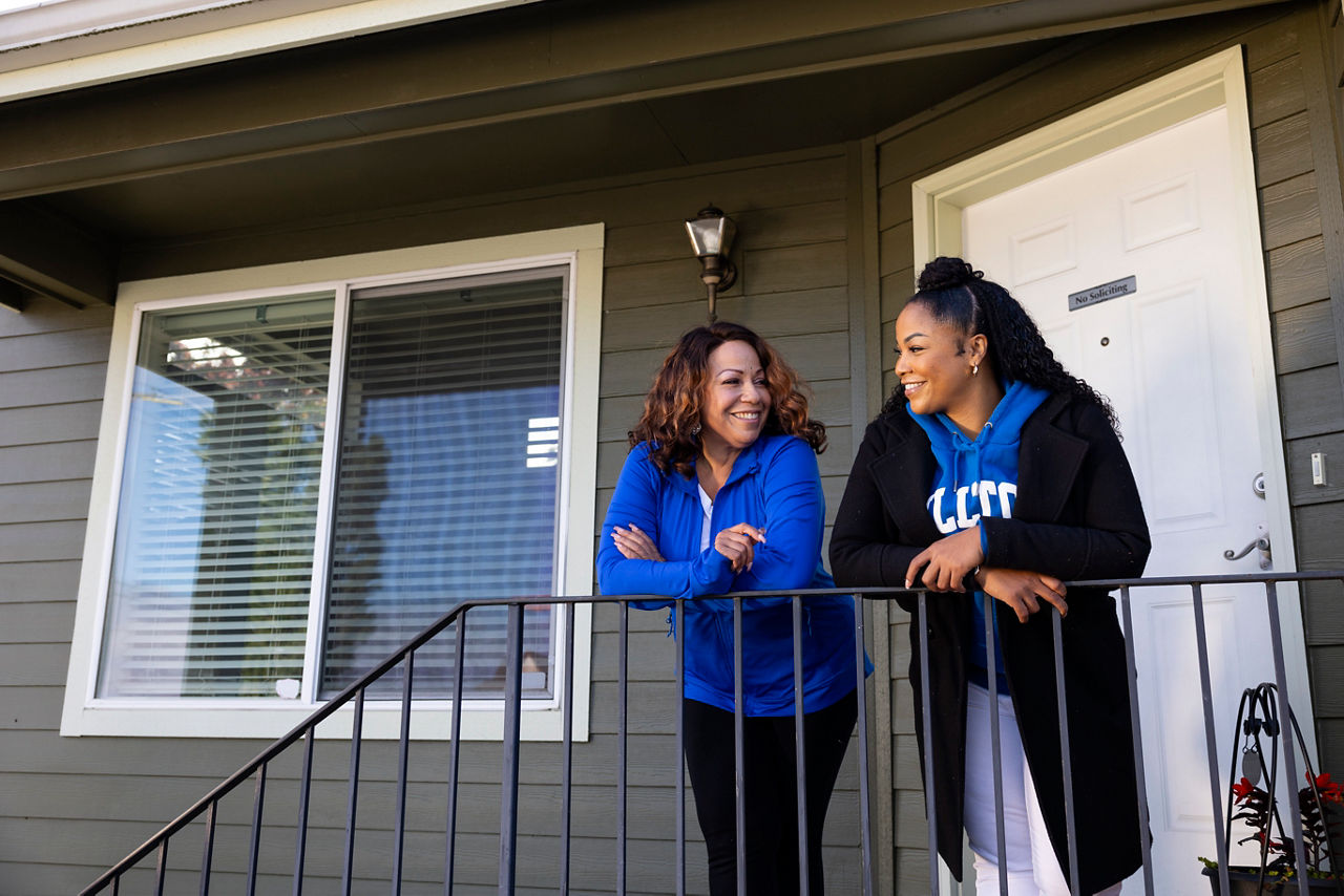 Two women standing and talking to each other on a front porch.