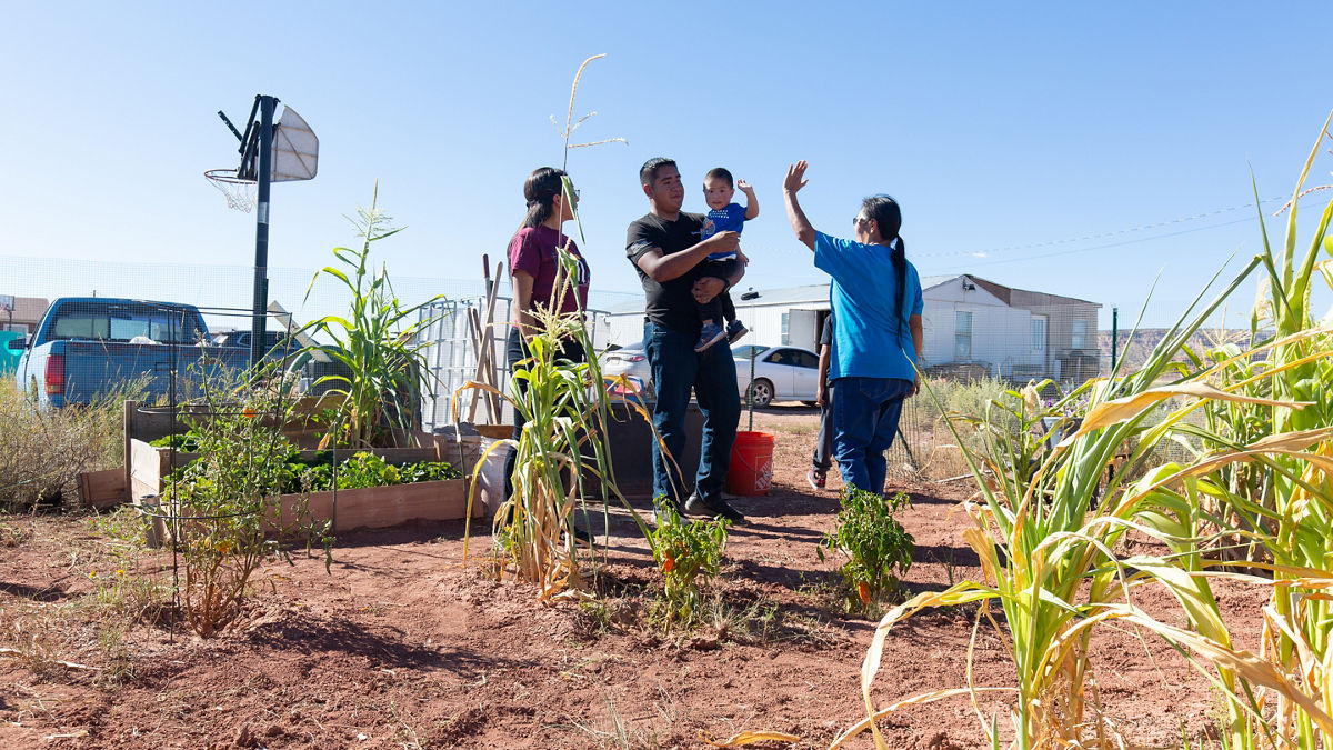 A group of people standing outside in a garden. One adult holds a child.