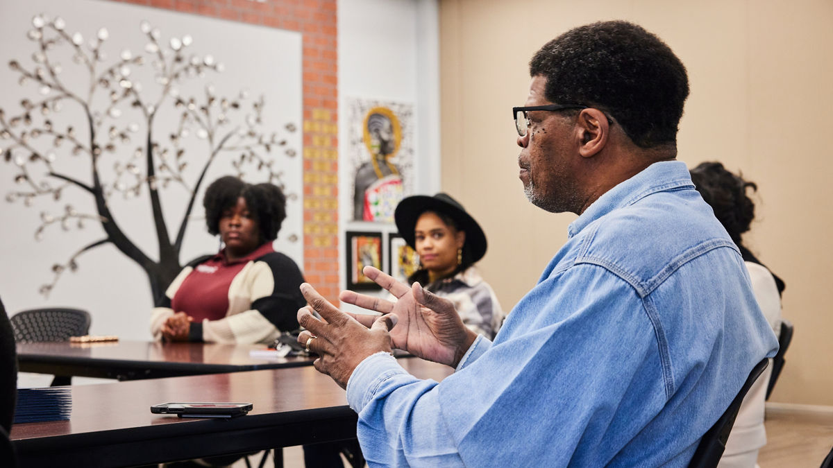 Man seated at a table speaks to young leaders.