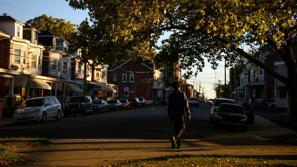 A teen walking across a street toward a sidewalk.