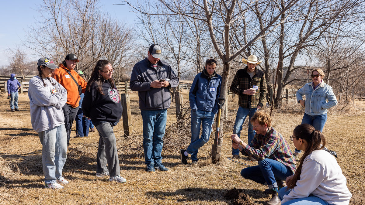 A group of people stand outside in a circle examining a soil sample.