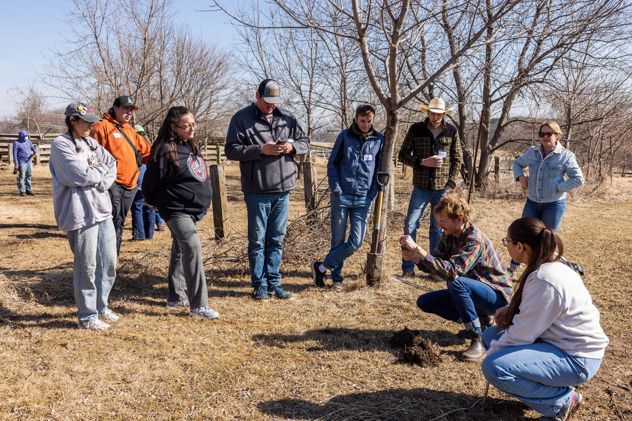 A group of people stand outside in a circle examining a soil sample.
