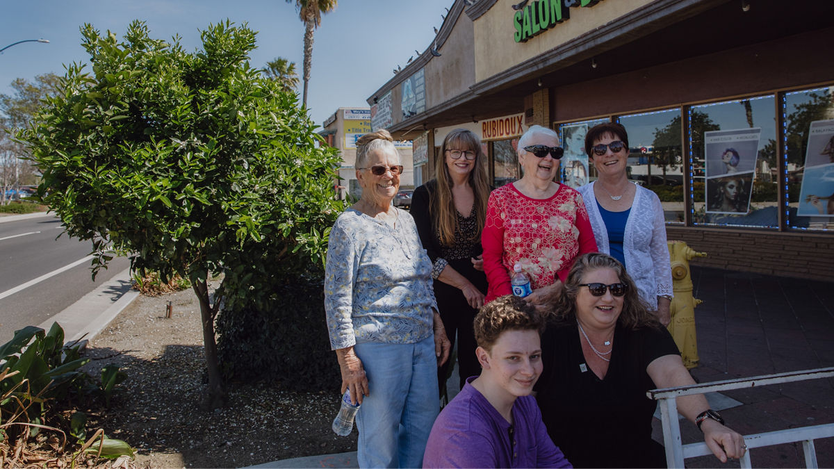 Six people pose for a portrait next to a lemon tree growing outside a storefront.
