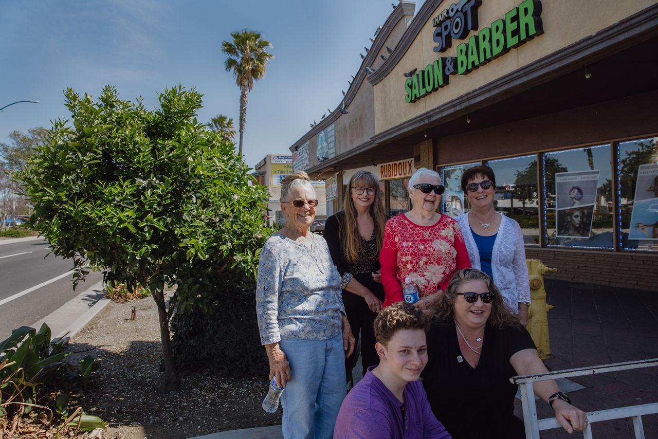 Six people pose for a portrait next to a lemon tree growing outside a storefront.