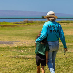 A woman in a straw hat stands near a body of water with her granddaughter.