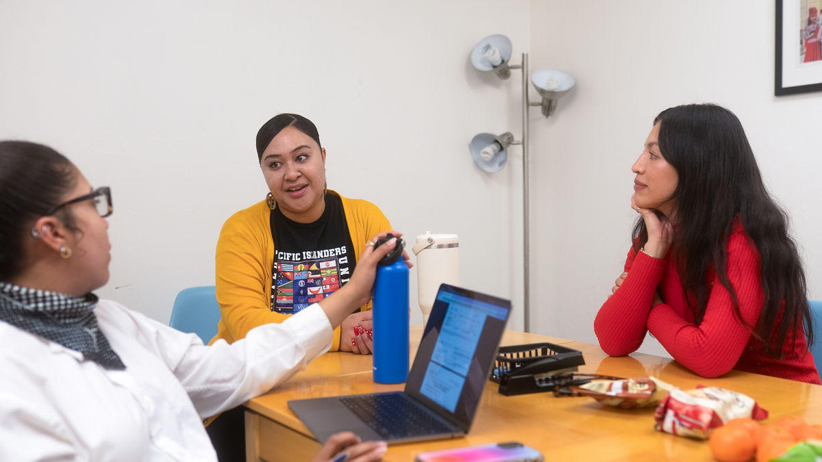 Three women sit and talk at a conference table.