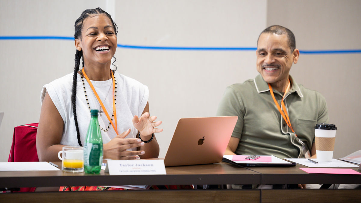 A woman and man smiling while looking at a laptop on a conference table.
