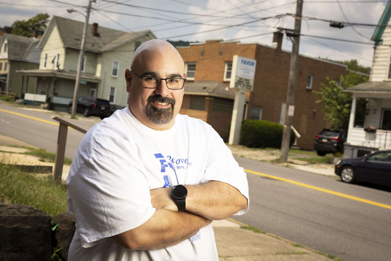 A man standing near a sidewalk with his arms crossed.