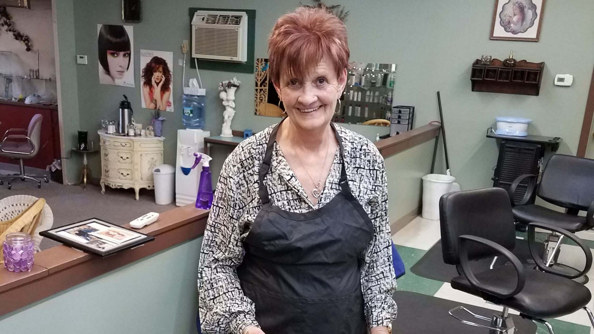 A woman standing behind a chair at a hair salon.