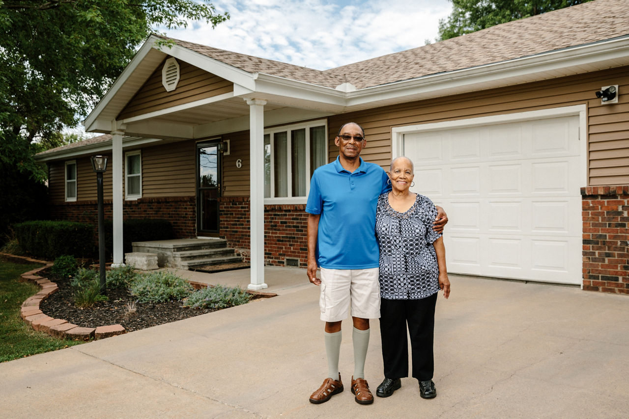 A couple standing in their driveway at home.