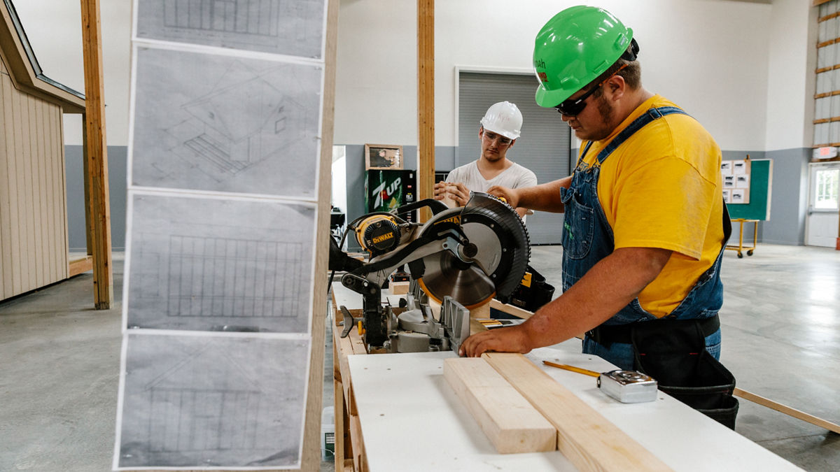 Two men cutting wood with a table saw. 