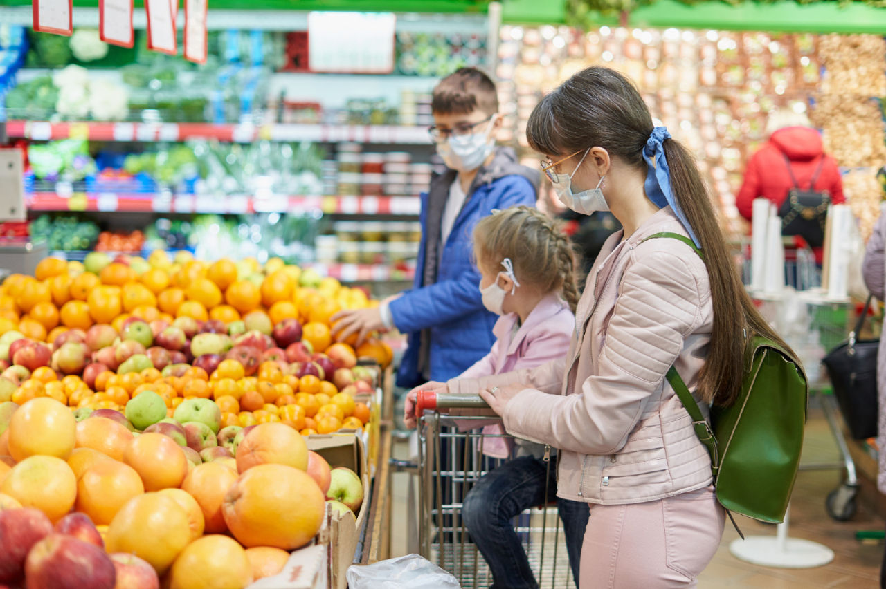 Mom with children in protective masks choose fruits to buy in the store.