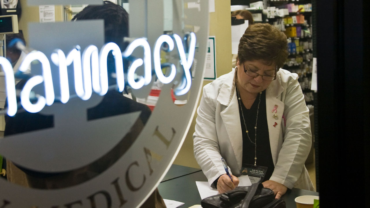 A pharmacy window, showing a pharmacist inside filling in paperwork.