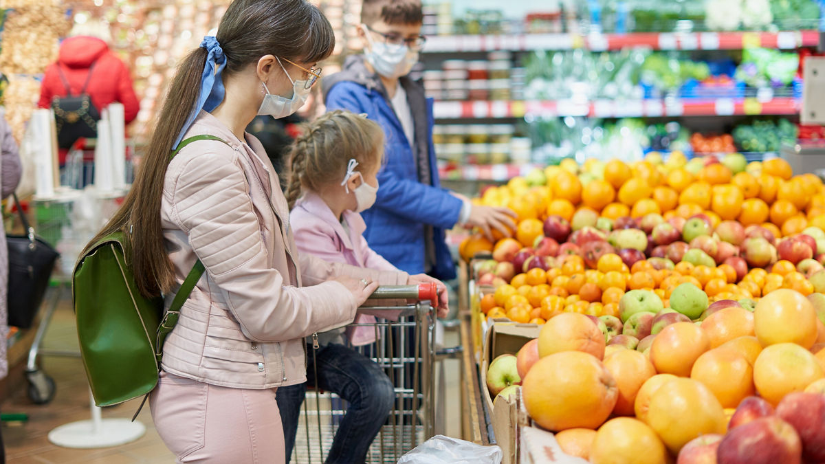 Mom with children in protective masks choose fruits to buy in the store. IStock 1285517923