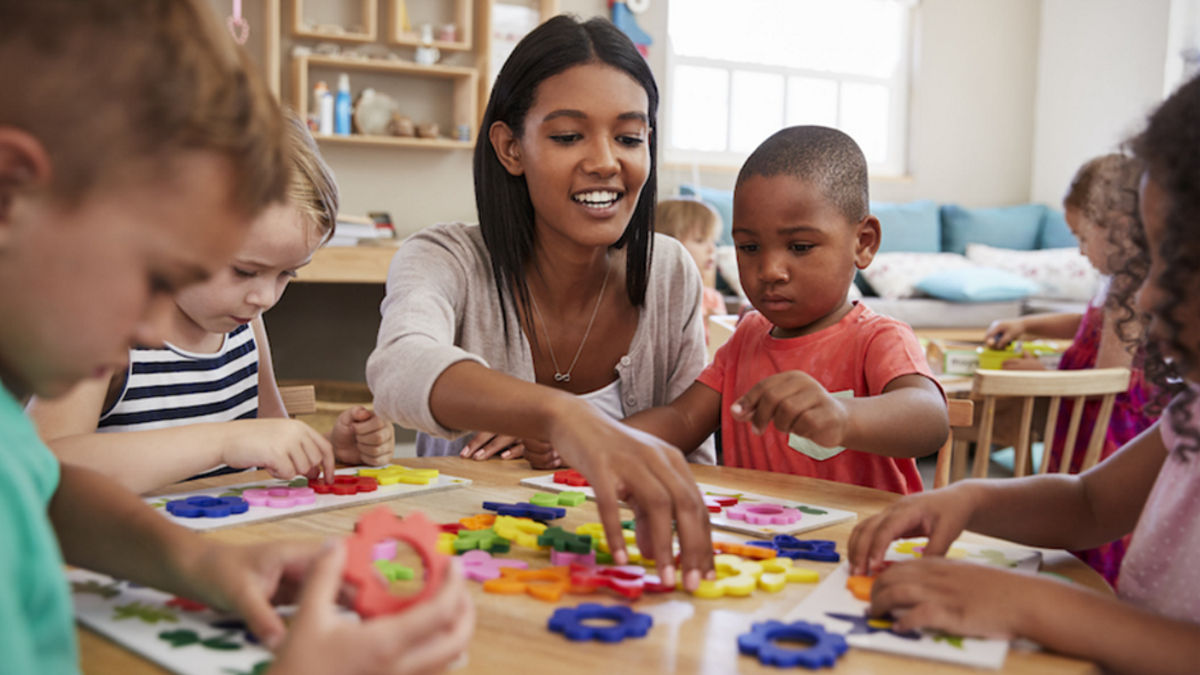 A daycare provider laying a game with children at a table.