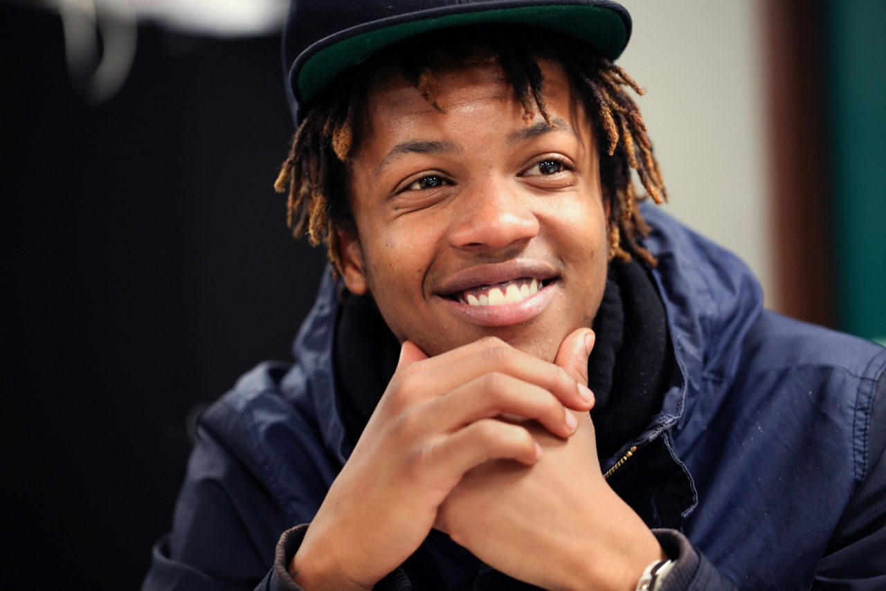 A young man in a baseball cap smiling.