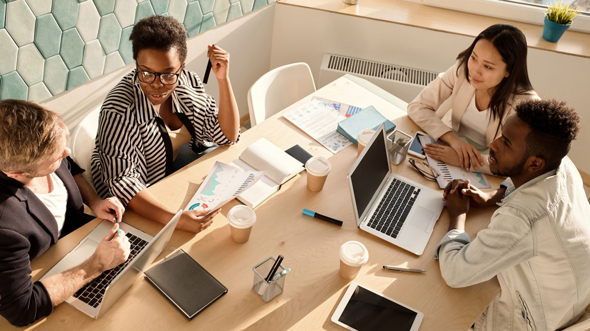 Four young, multi-racial professionals engaging in an office meeting.