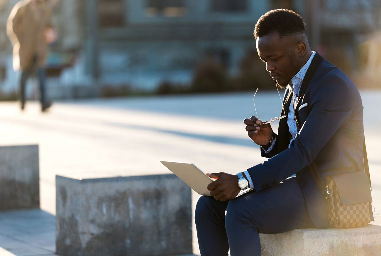 African american business man sitting on a bench of the city working with his laptop