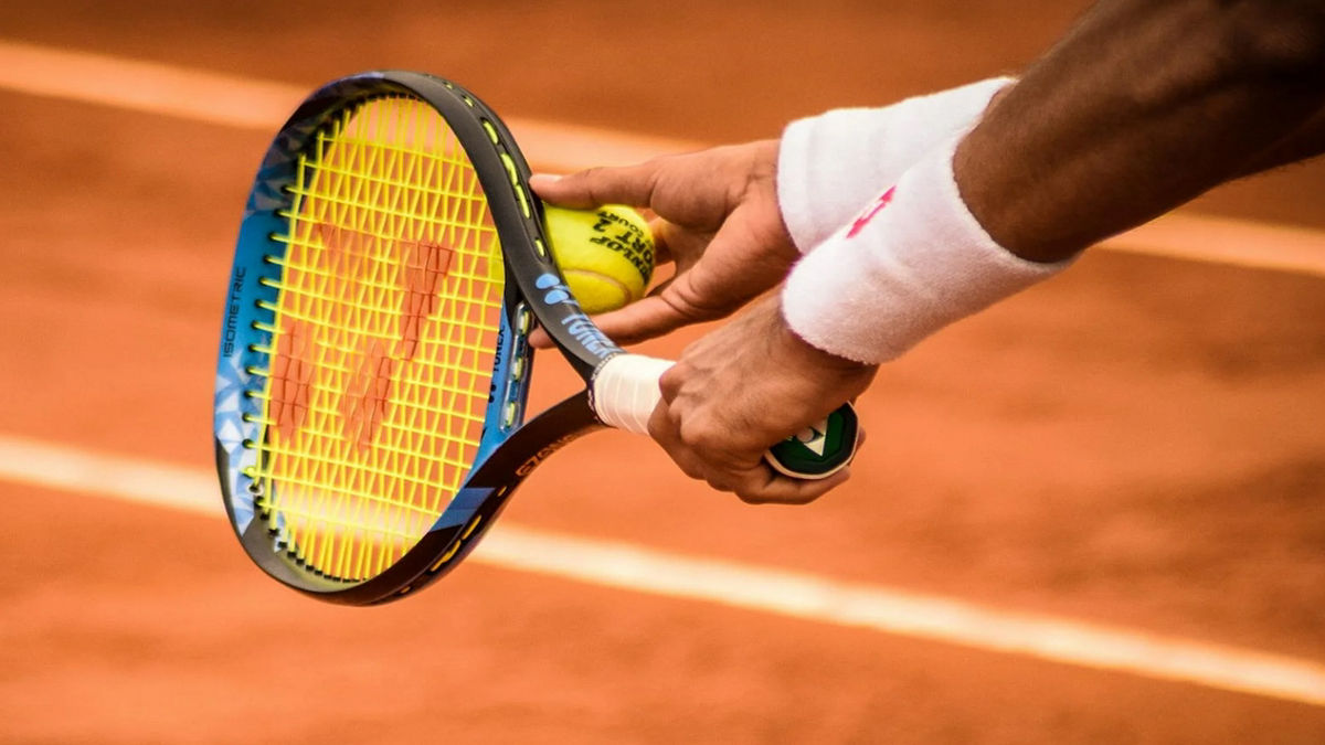 A person's hands are shown holding a tennis racket and tennis ball.
