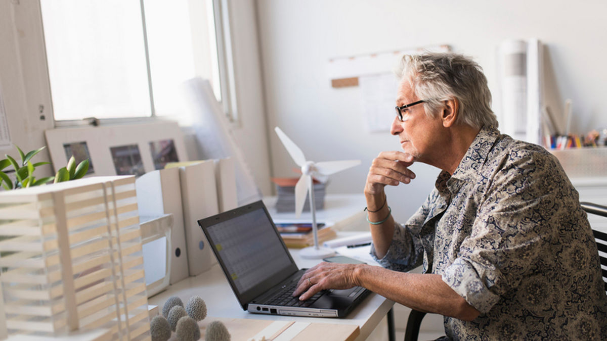 Older man working in office on laptop.