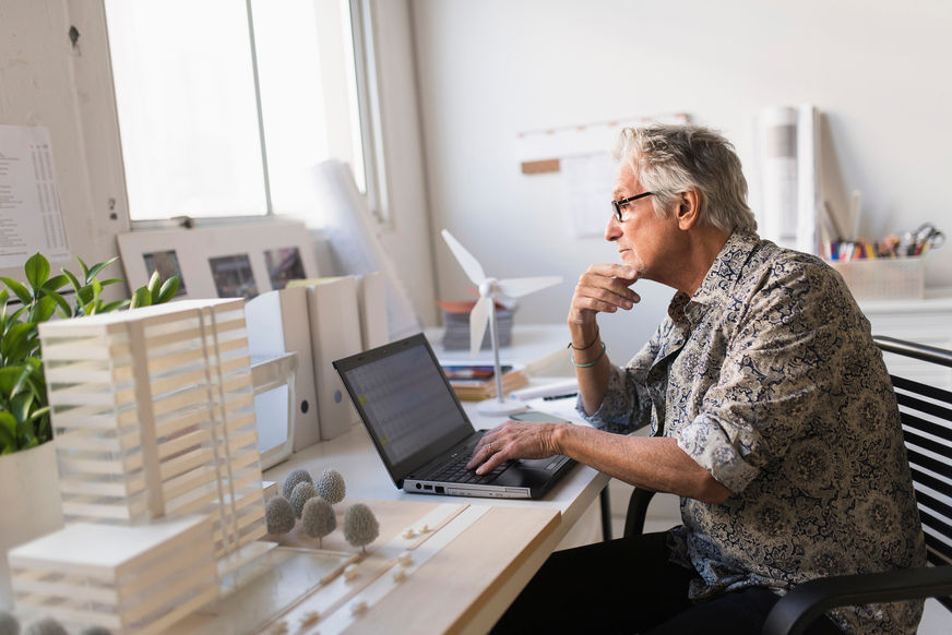 Older man working in office on laptop.