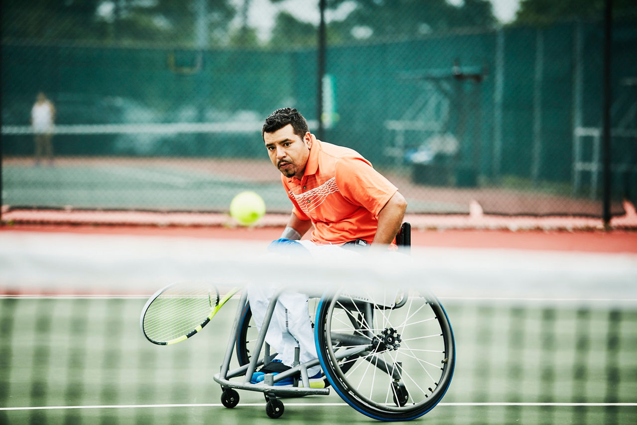 An adaptive man playing tennis during wheelchair tennis match.