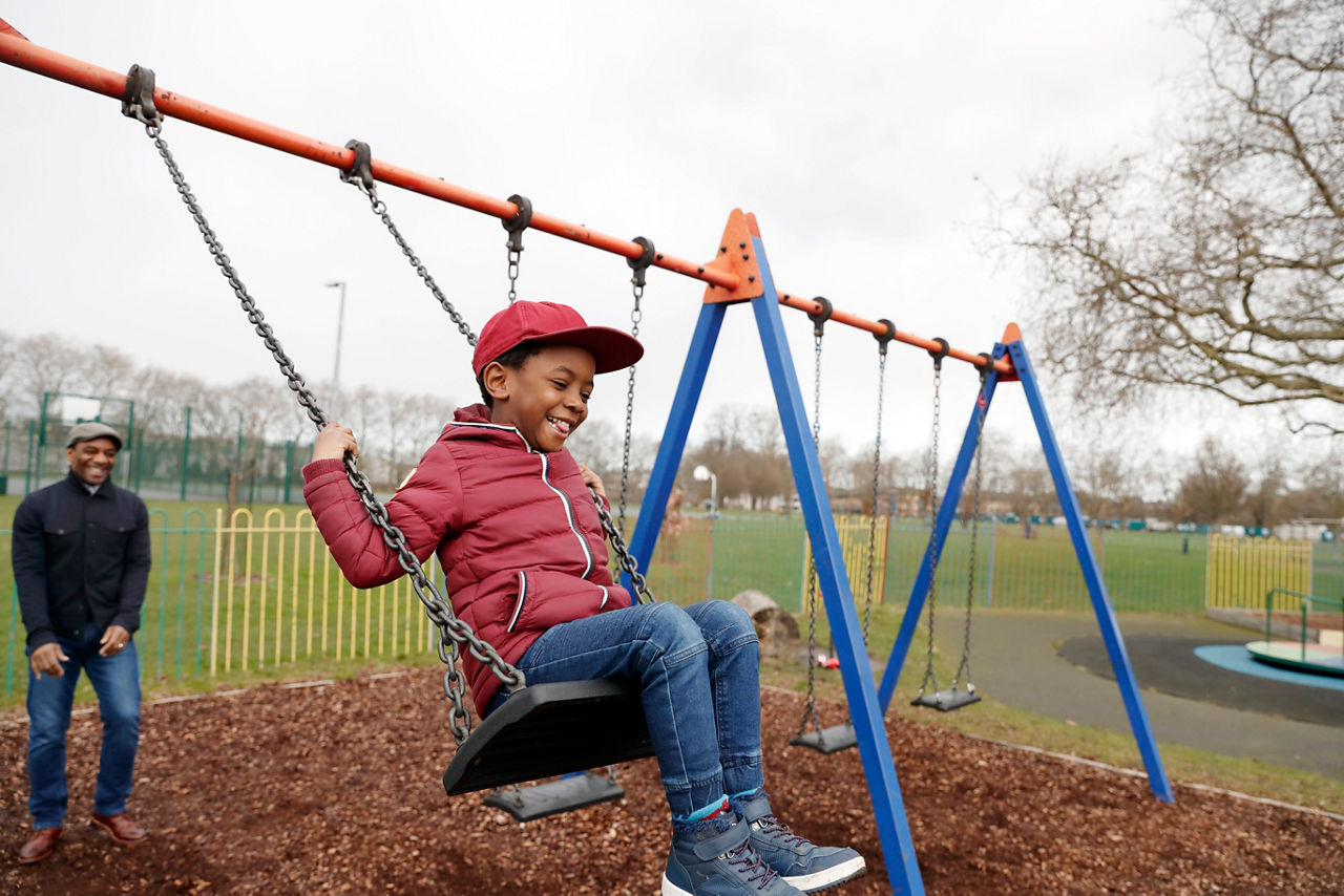 A father and son playing on the swings in the park.