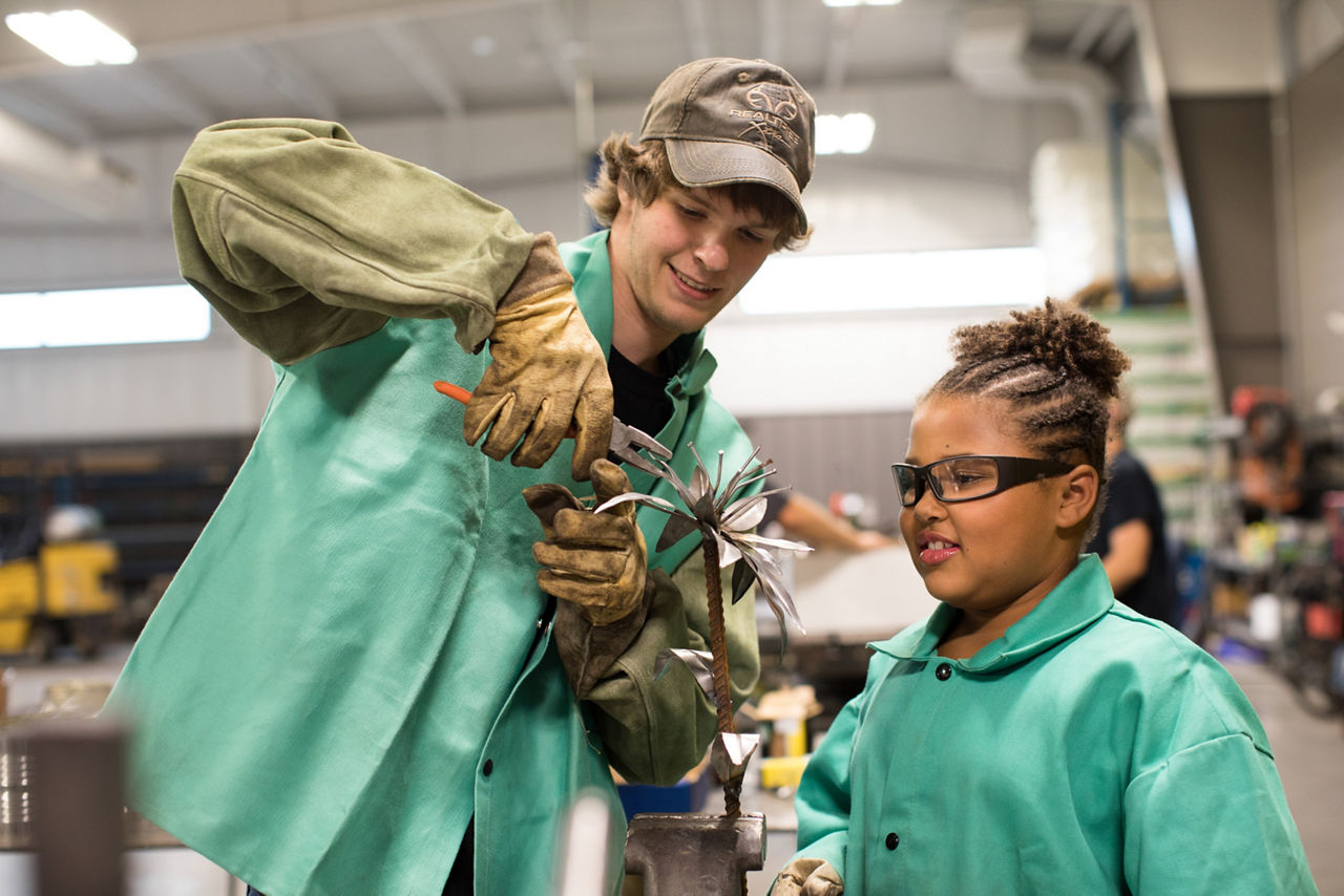 A teenager showing a fellow student how to use tools in metal class.