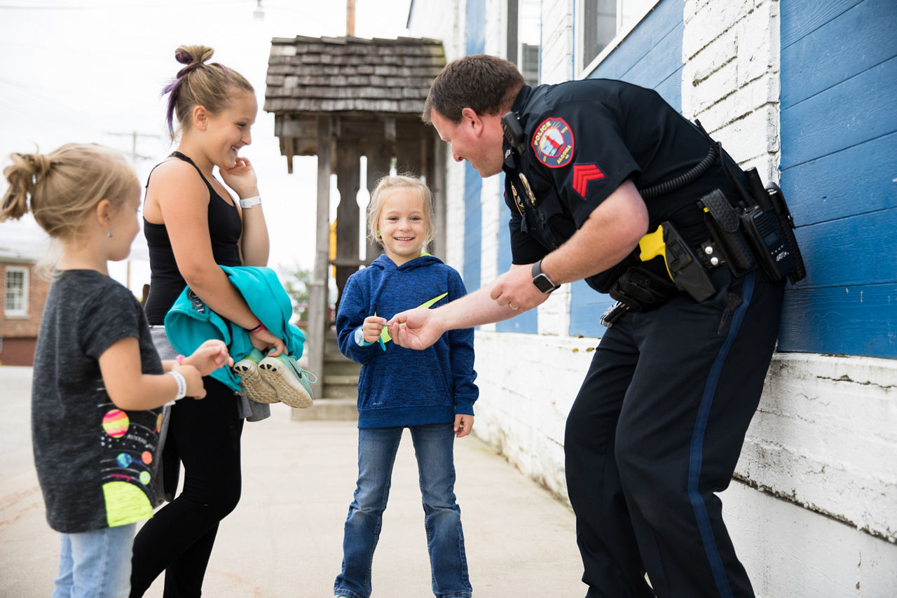 A policeman hands out stickers to three girls. 