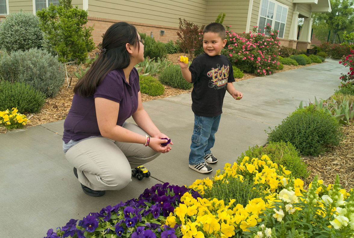 Young woman with a little boy outside a Green House residence in San Angelos, Texas. They are looking at the flowers.